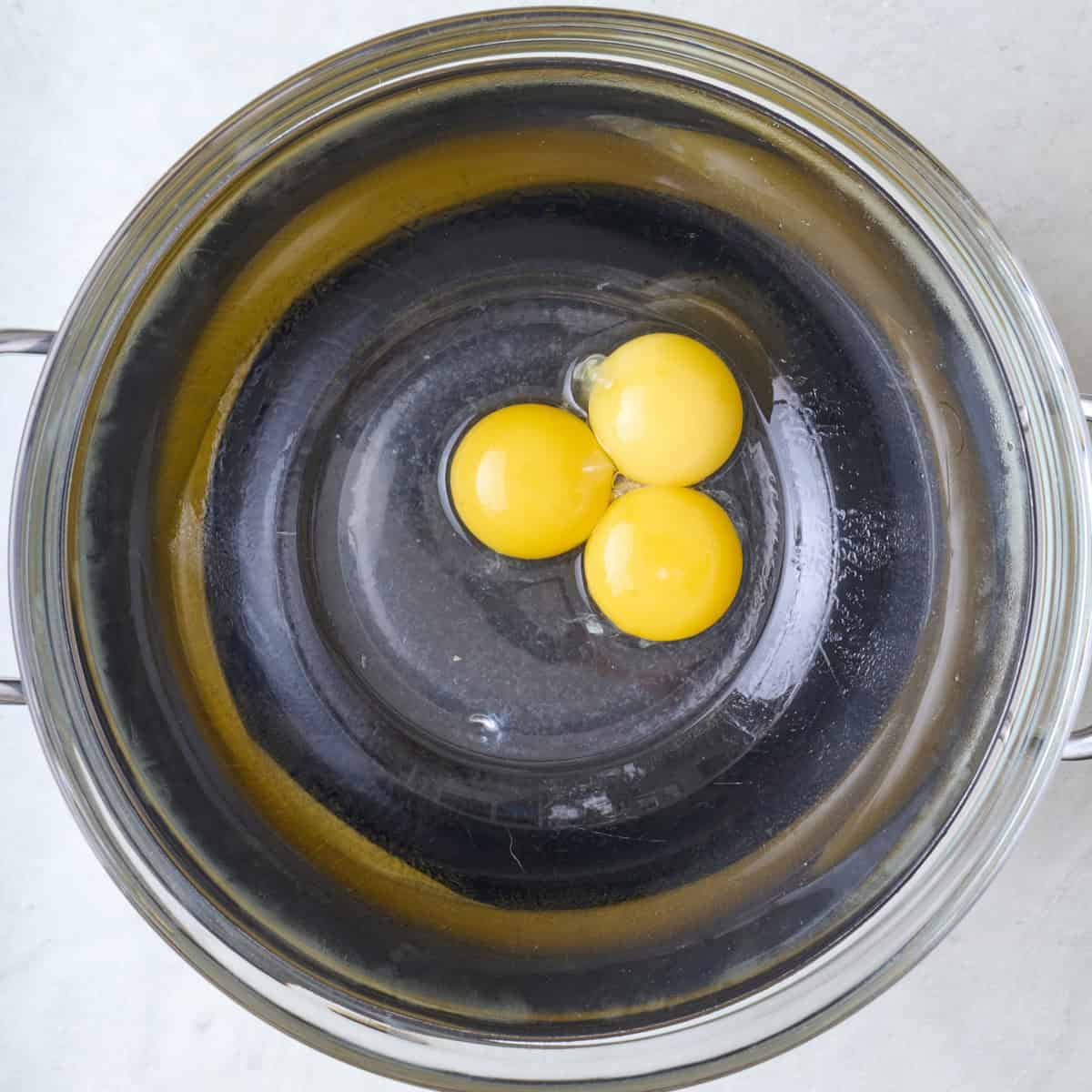 Egg yolks, water and lemon juice in a heat safe bowl over a pot of water before whisking.