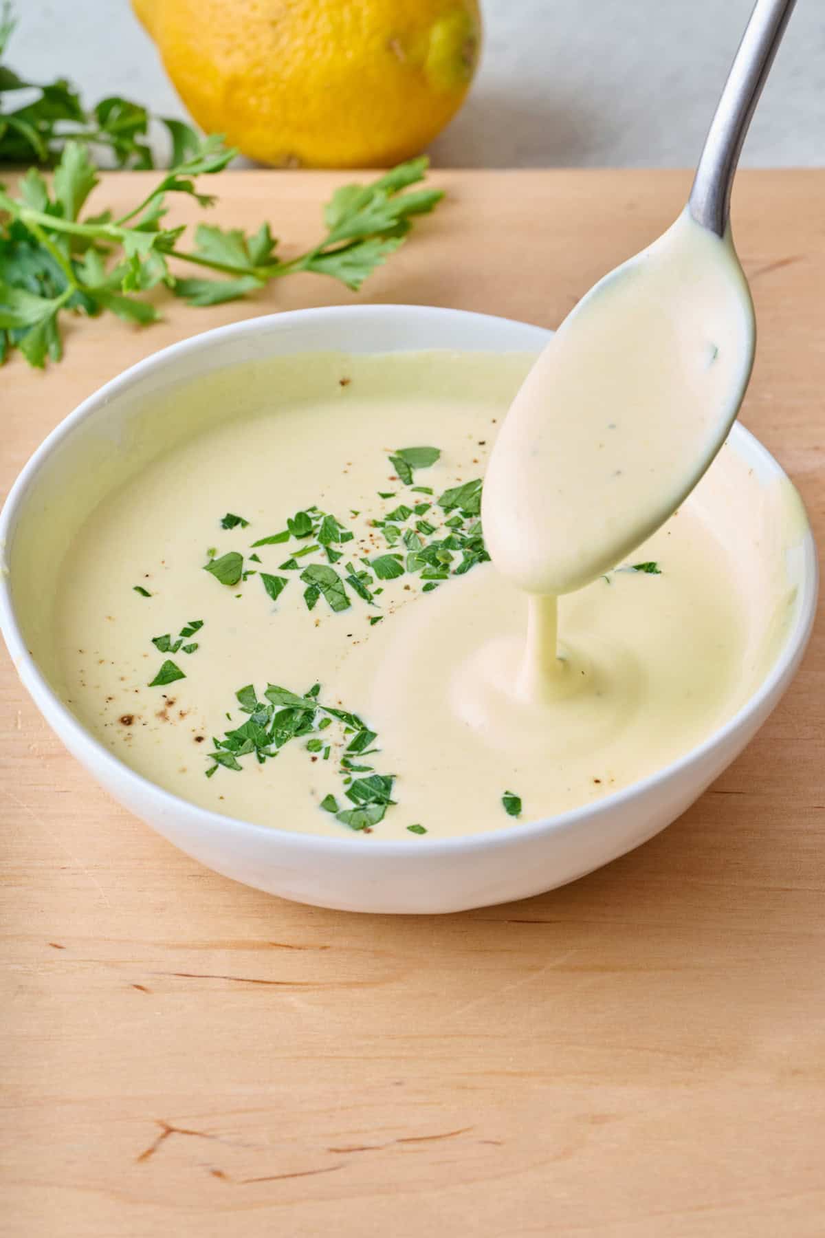 Hollandaise sauce in a bowl with a spoon drizzling the silky sauce back into the bowl.