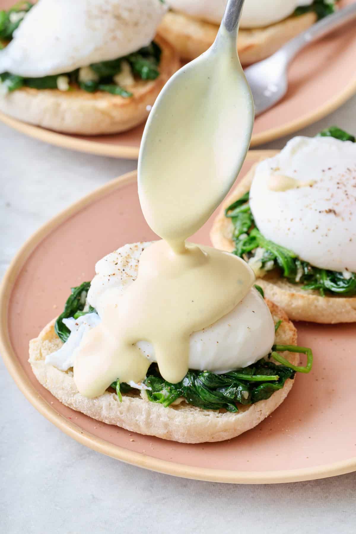 Eggs Florentine on a plate with homemade hollandaise sauce being drizzled on top of the poached egg.