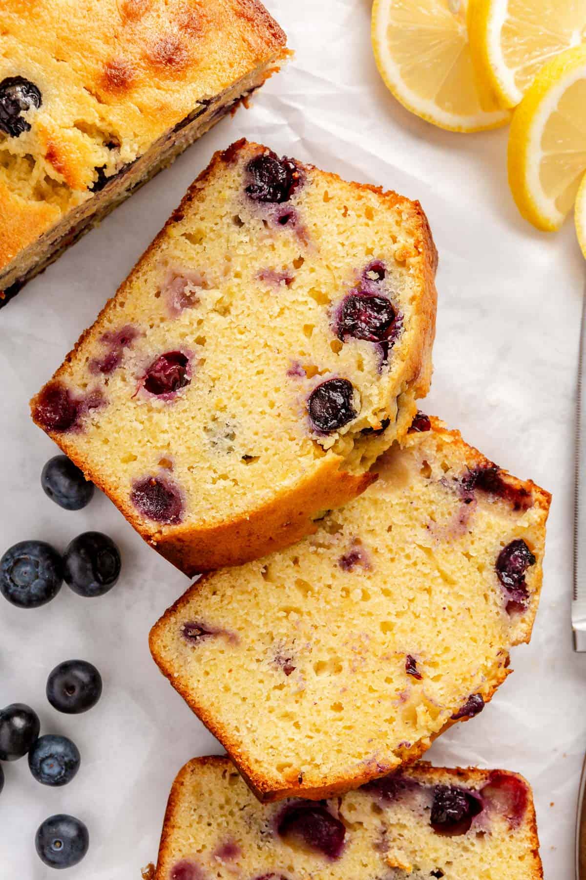 A few slices of lemon bread with blueberries on parchment paper, fanned out to show thick, moist slices.