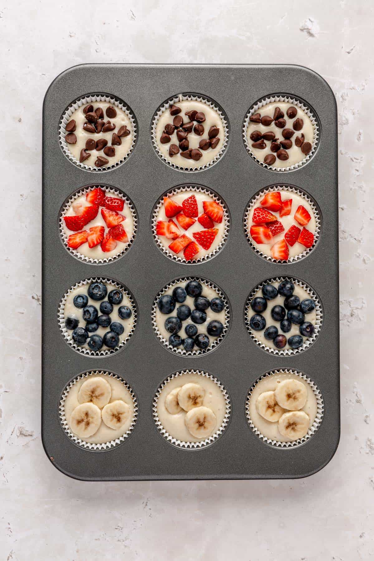 Batter divided into a 12 cup muffin tin with toppings added on top, before baking.