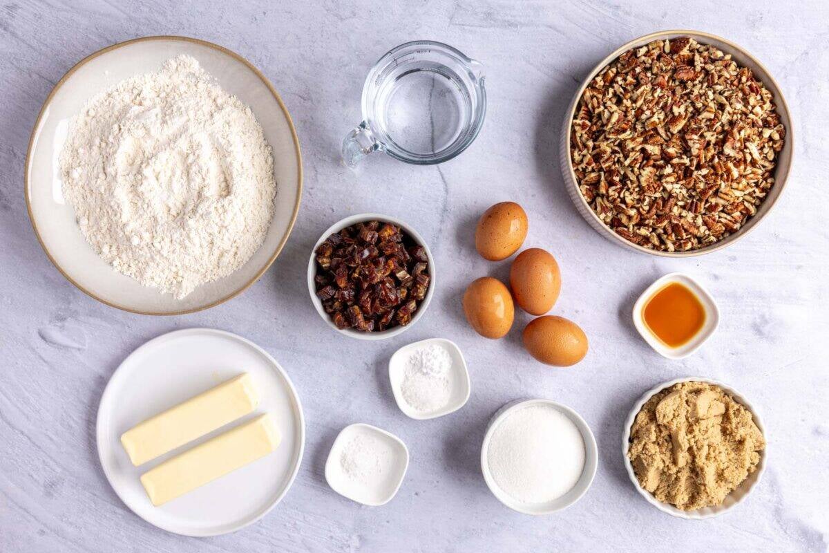 Ingredients for dessert recipe: flour, pecans, water, dates, butter, baking soda, salt, eggs, sugar, brown sugar, and vanilla extract.