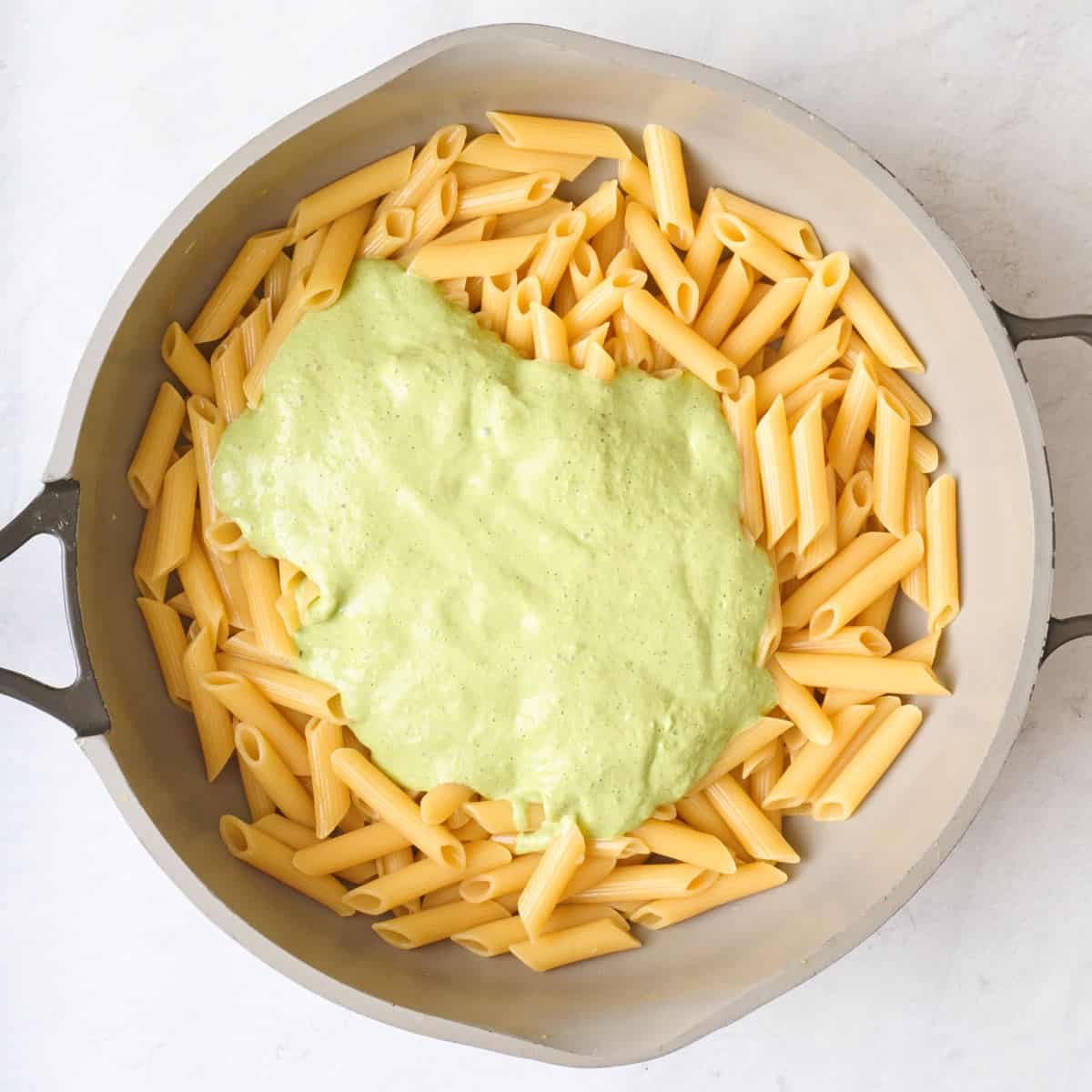 Cooked penne in pot with green sauce added on top before combining.