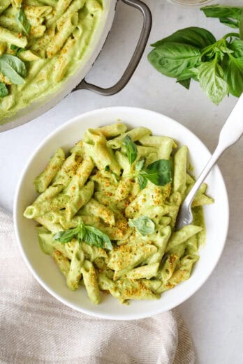 Creamy pistachio penne pasta in a bowl garnished with crushed pistachios with pot of more pasta nearby.