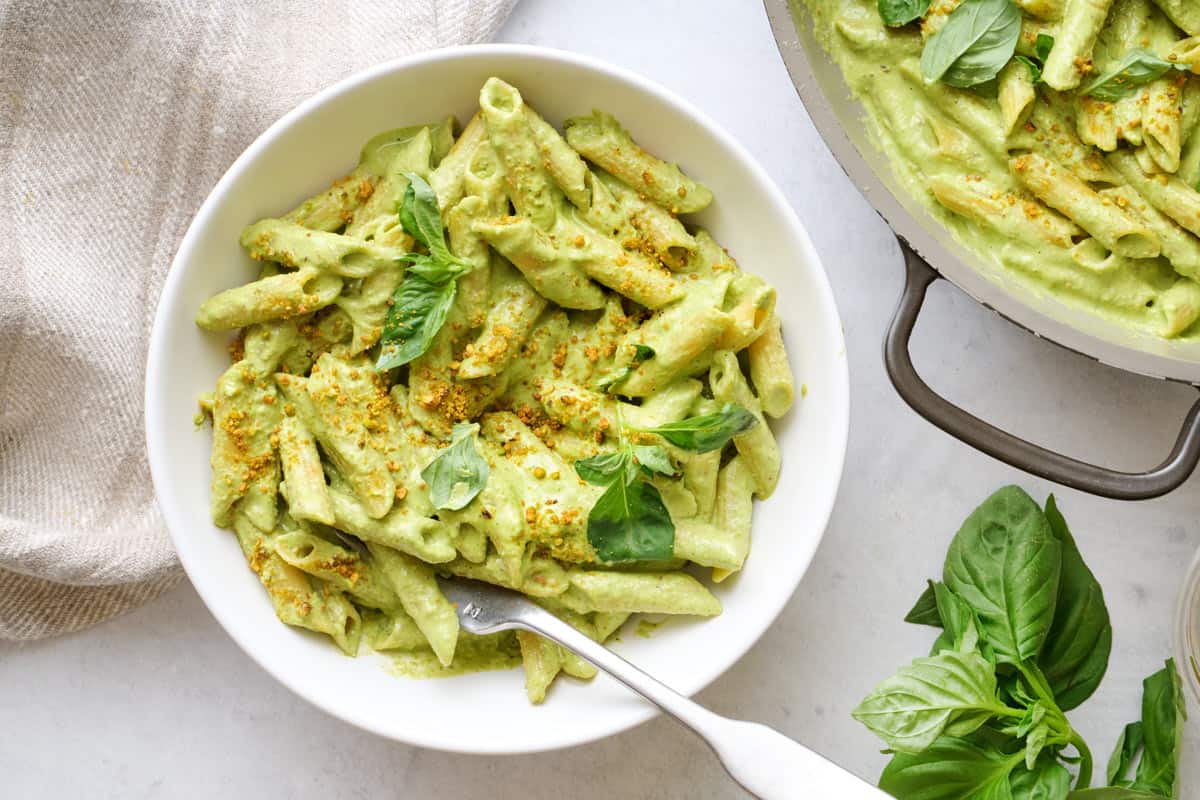 Bowl of green pistachio pasta sauce tossed with penne pasta in a bowl.
