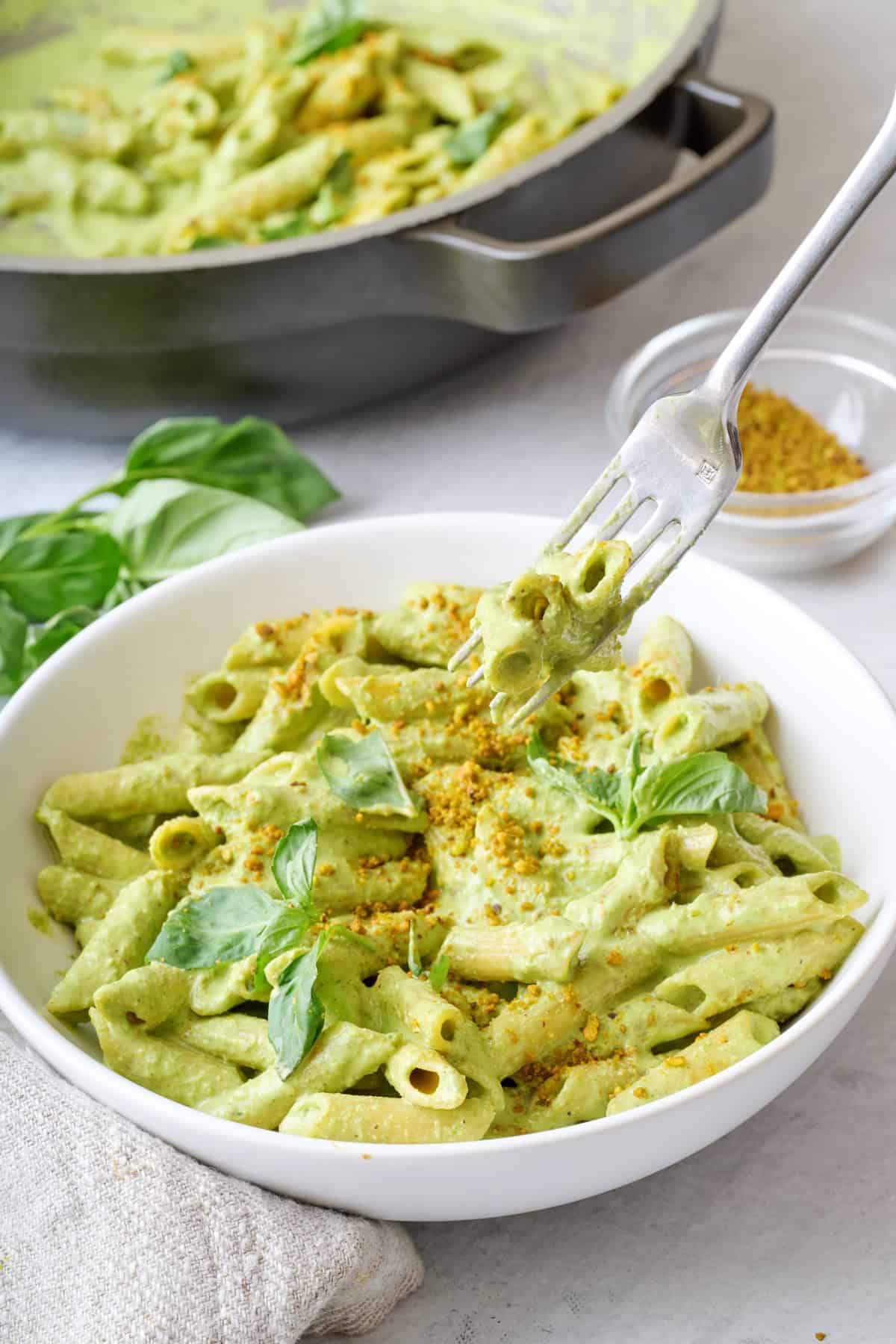 Fork lifting up a bite of creamy pistachio pasta from a bowl.