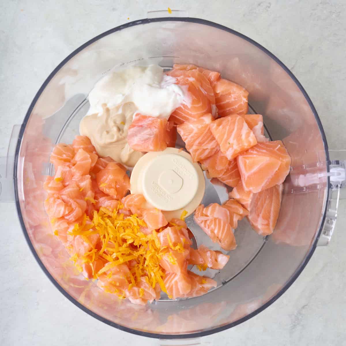 Pieces of salmon, yogurt, mustard, and lemon zest in the bowl of a food processor.