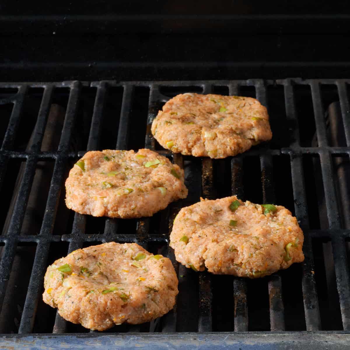 Four salmon burgers cooking on a grill.