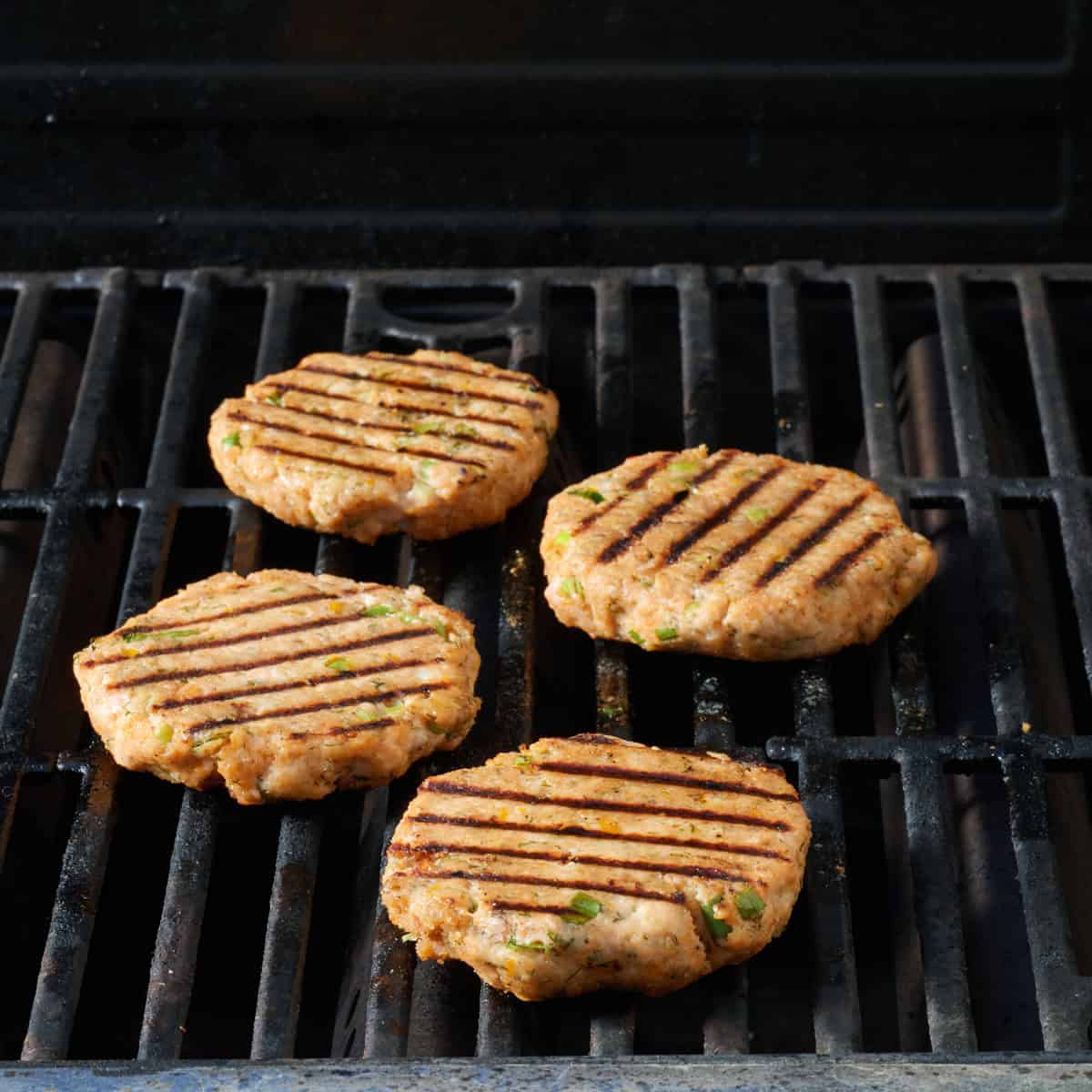 Four cooked salmon burgers on a grill.