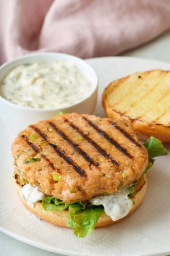 Open faced burger with small dish of tartar sauce on plate.