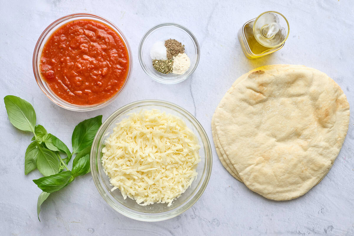 Ingredients for recipe, marinara sauce, fresh basil, shredded mozzarella cheese, spices, oil, and pita bread.