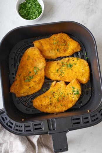 Breaded chicken in an air fryer basket, garnished with fresh parsley.