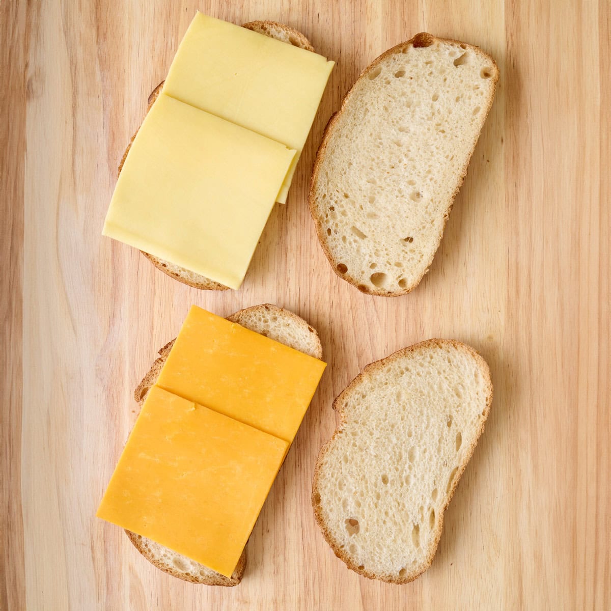 4 slices of bread on a cutting board with 2 slices of cheese on two pieces of bread.