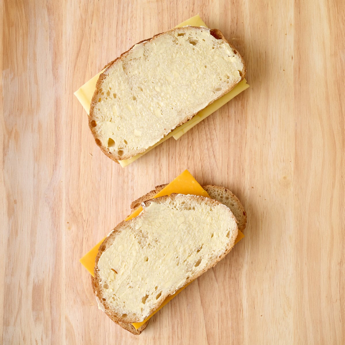 2 sandwiches with cheese on a cutting board with butter added on top.