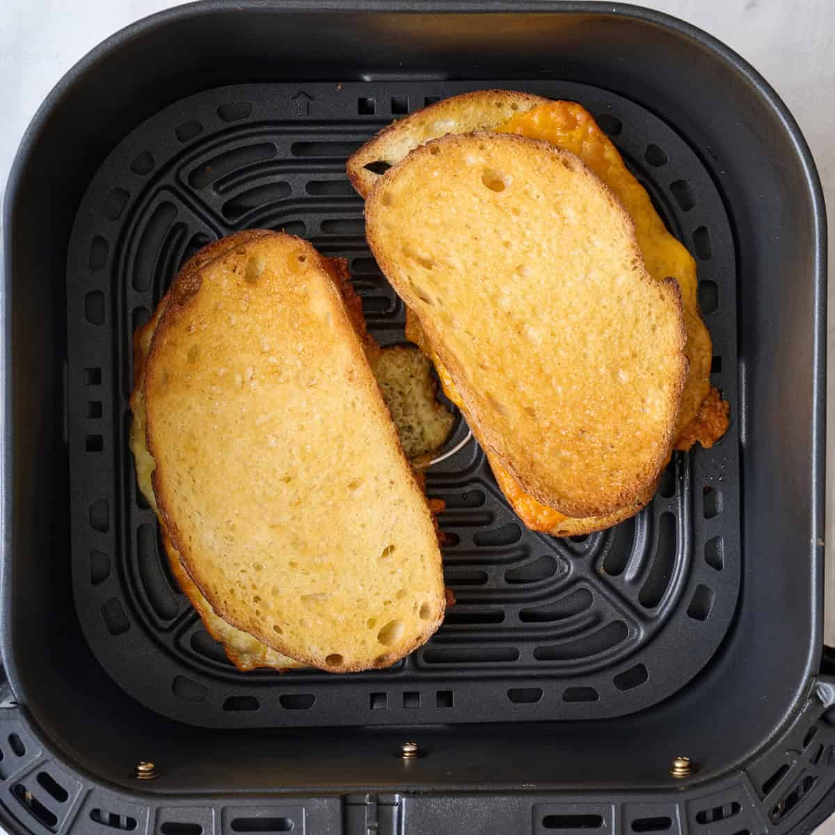 2 sandwiches in an air fryer basket after cooking.