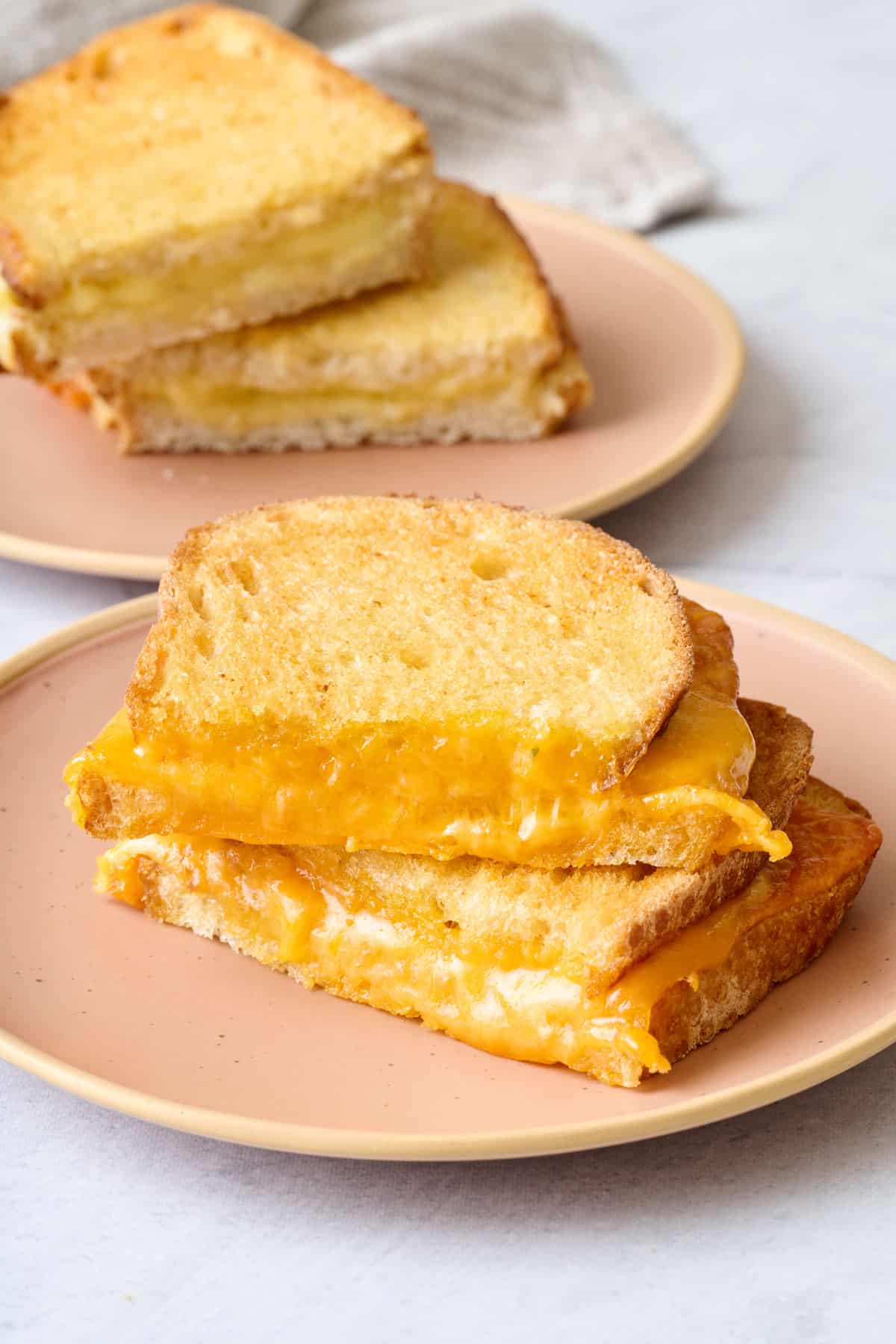 Two small plates with a cut air fried grilled cheese on each, with each cut propped on top of the other.