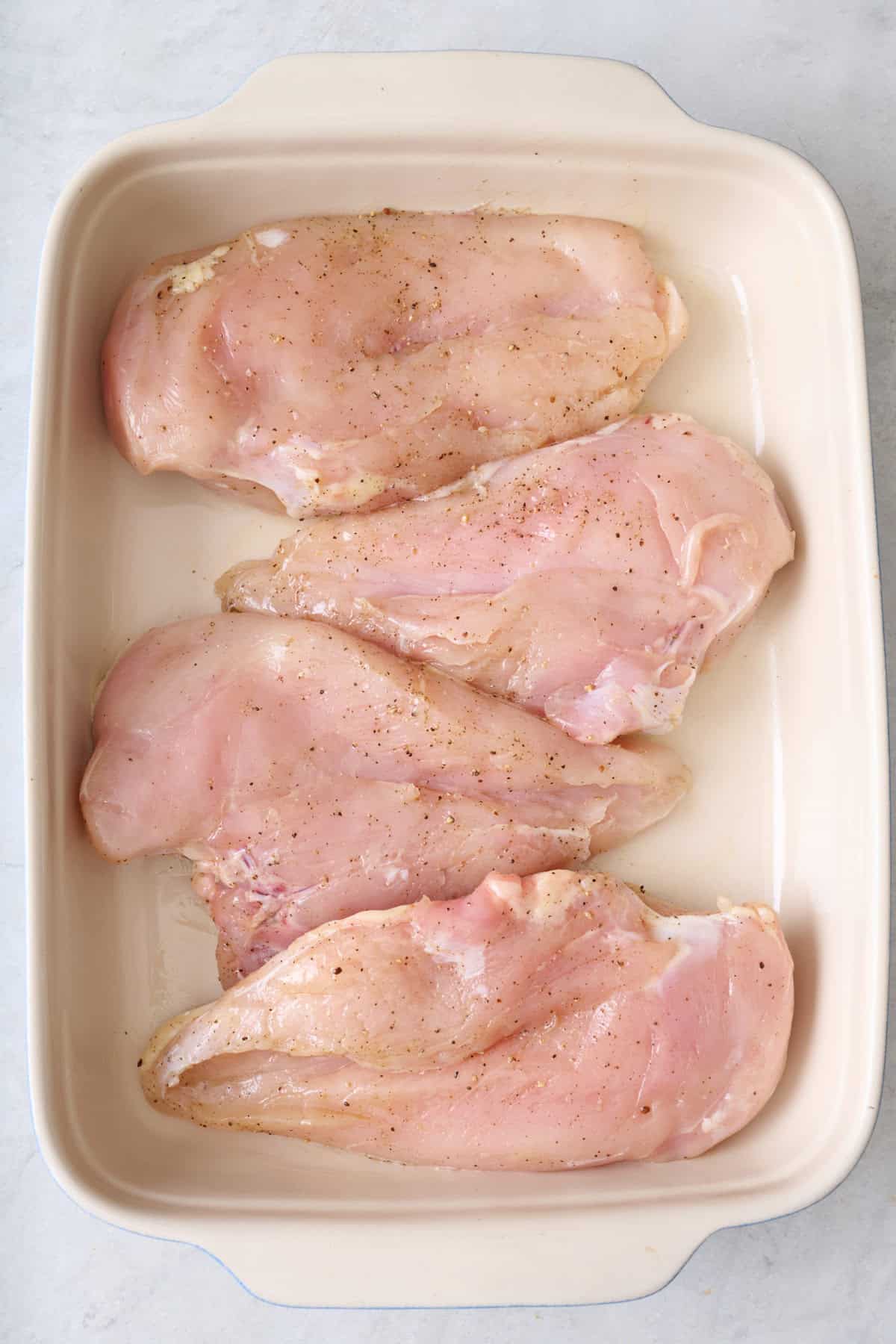 Chicken breast in a baking dish seasoned with salt and pepper.