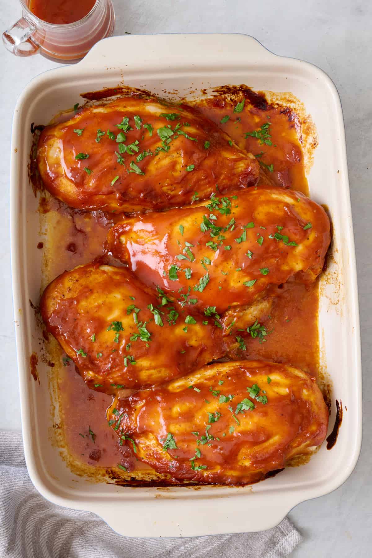 BBQ baked chicken breasts in baking dish, garnished with fresh parsley.