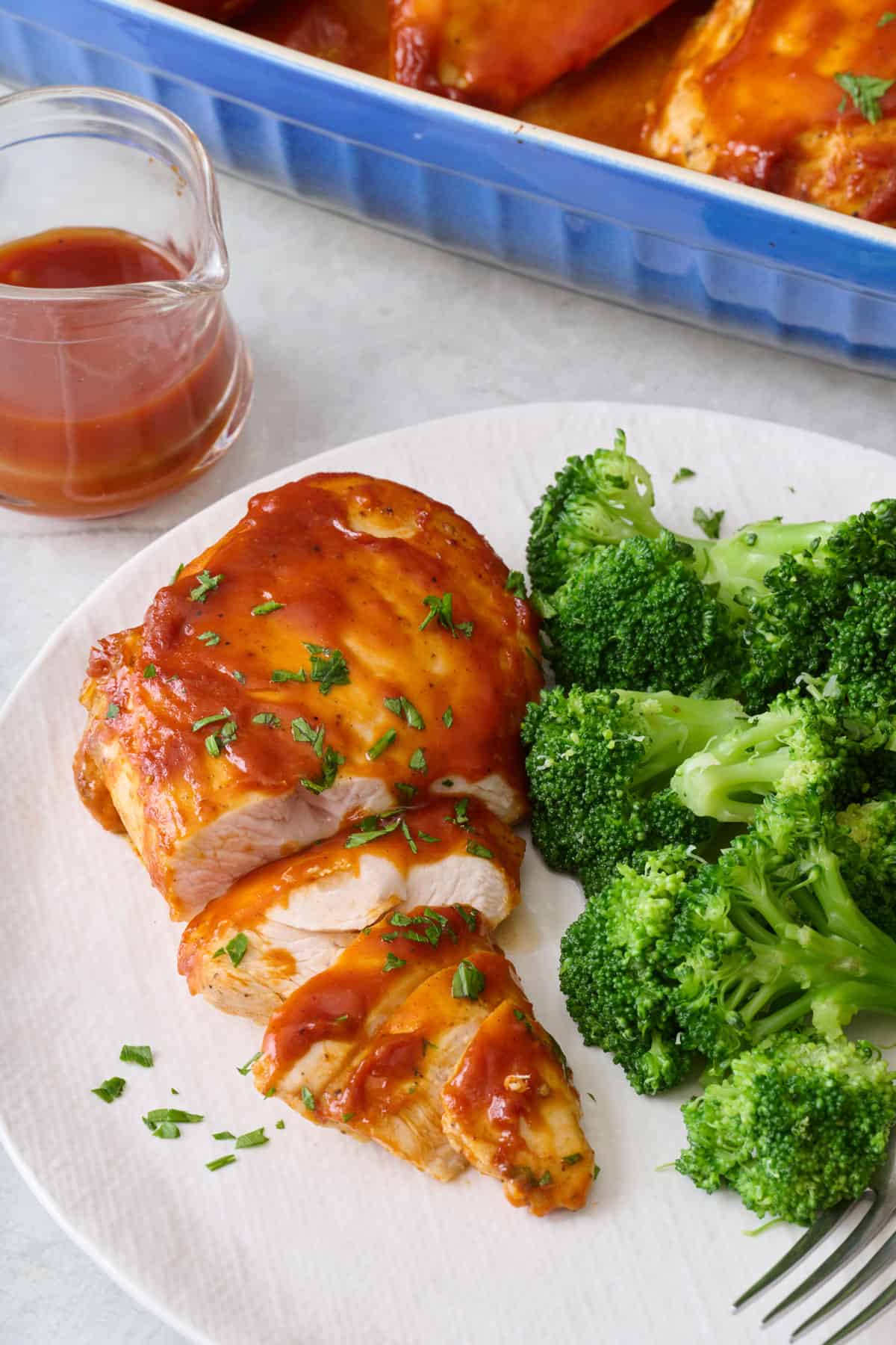 Baked barbeque chicken breast on a plate partially sliced on a plate with broccoli.