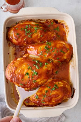 Spatula lifting up a bbq baked chicken from baking dish.