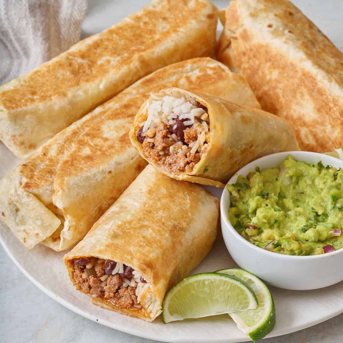 Seasoned ground beef burritos on a plate with a side of guacamole.