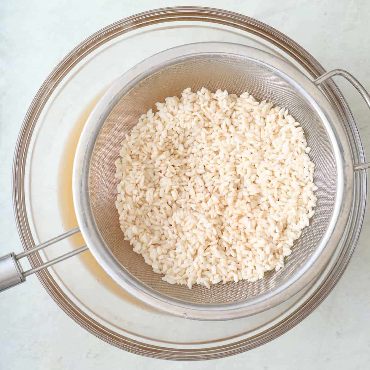 Rice in a fine mesh sieve over soaking liquid.