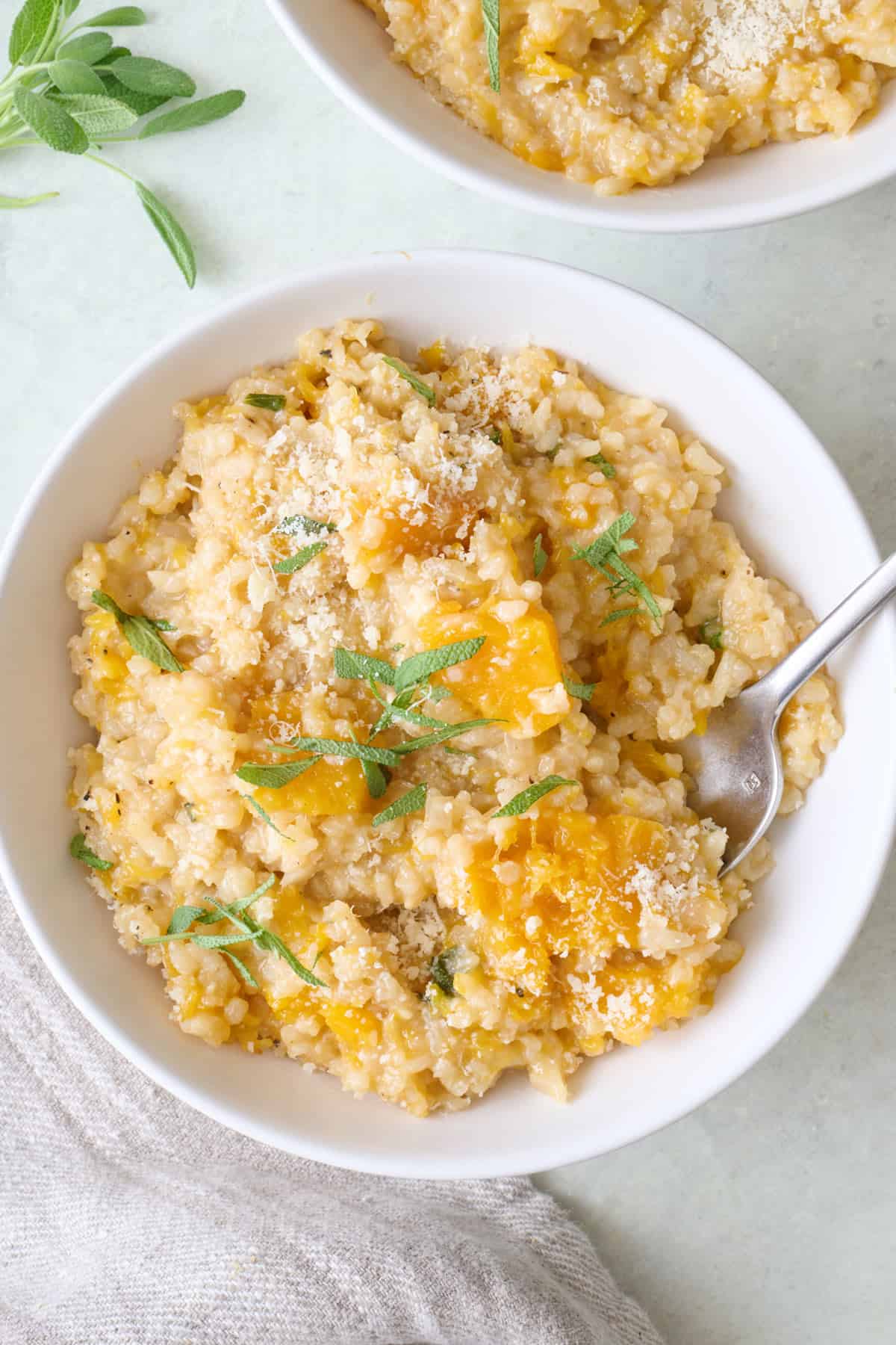 Butternut squash risotto in a serving bowl garnished with parmesan and fresh sage.