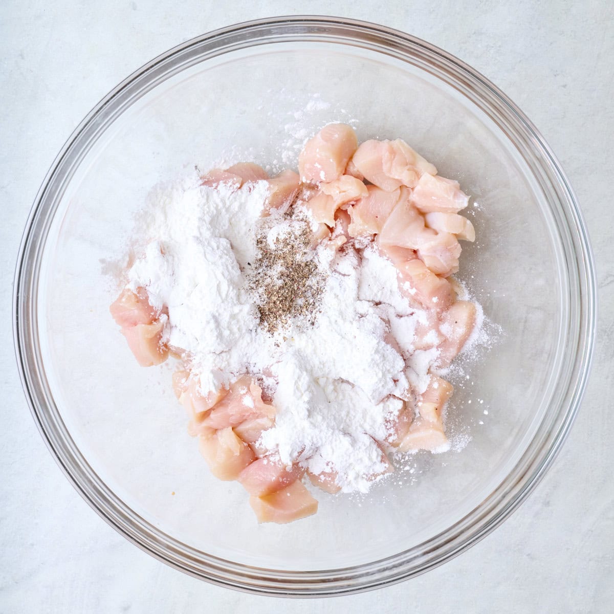 Chicken, salt and pepper in a bowl with cornstarch added.