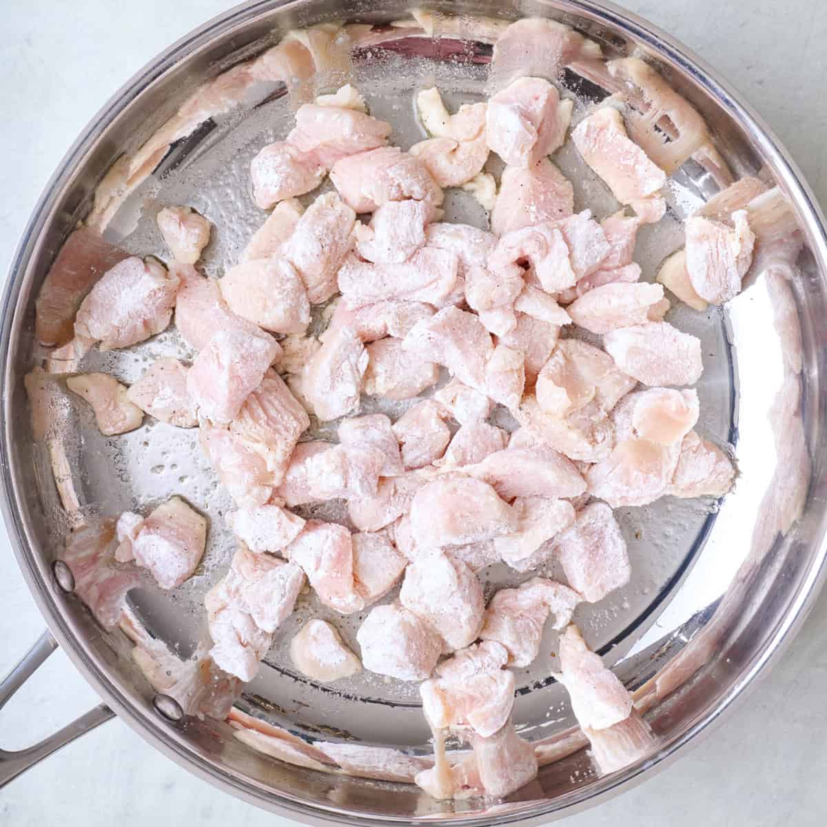 Cornstarch coated chicken in an oiled skillet.