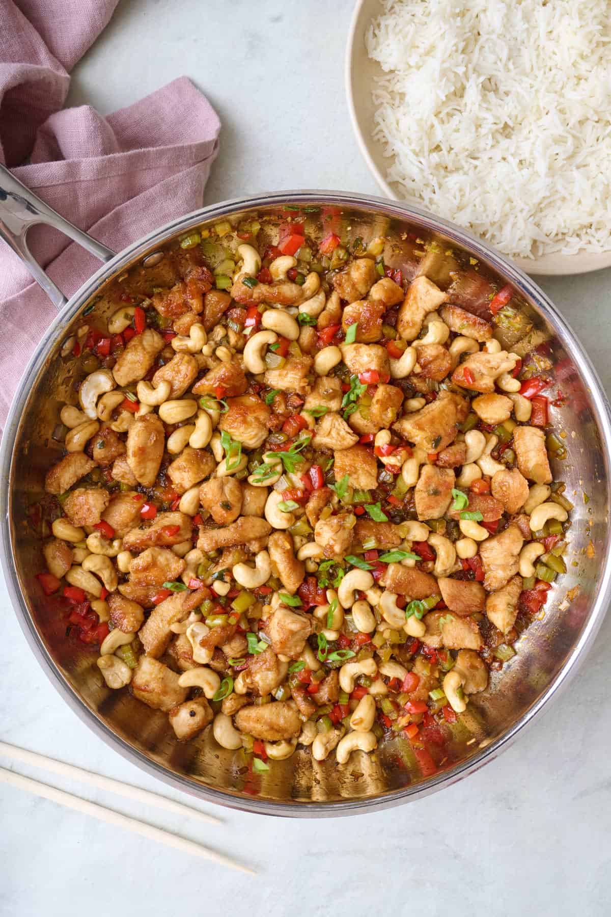 Cashew chicken in skillet with extra fresh green onions, small dish of white rice nearby.