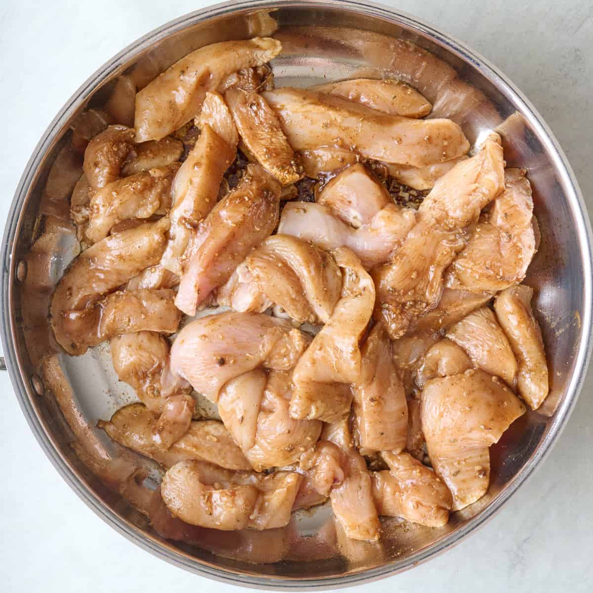 Seasoned chicken tenders in a skillet before cooking.