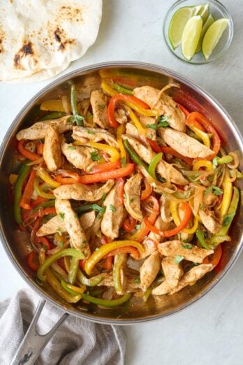 Stove top chicken fajita recipe in a skillet with tortillas nearby.