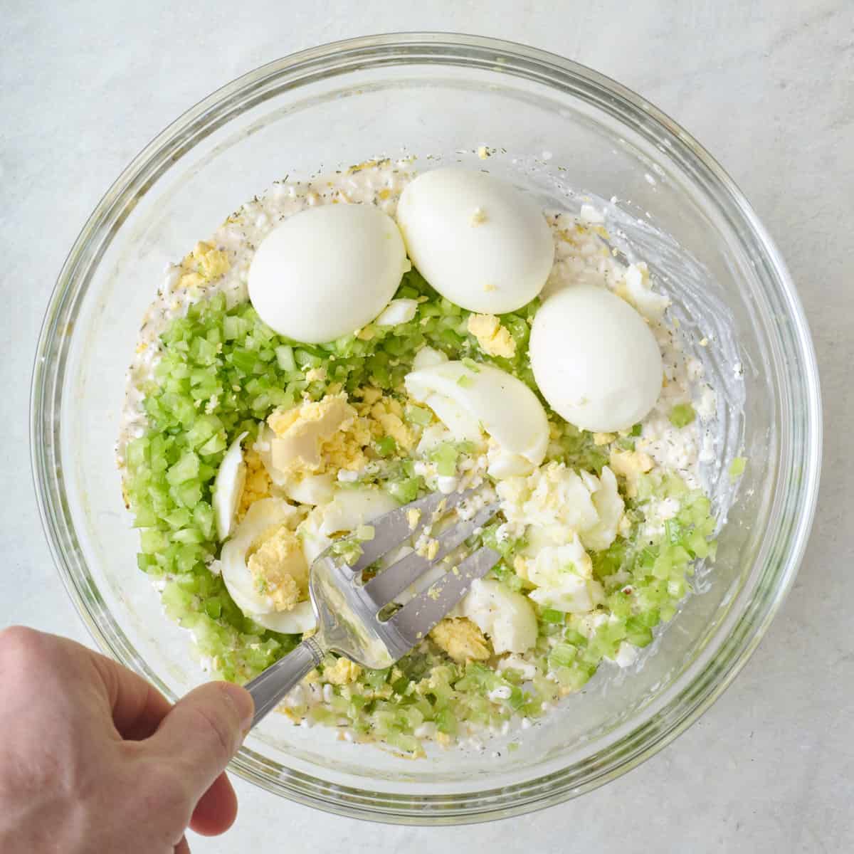 Fork starting to mash the dressing, eggs and dressing together.