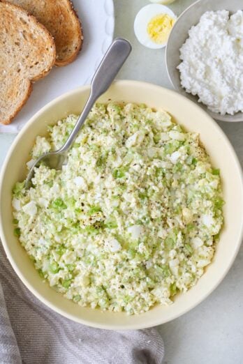 Cottage cheese egg salad in a bowl with a serving spoon dipped in, halved boiled egg and cottage cheese nearby.