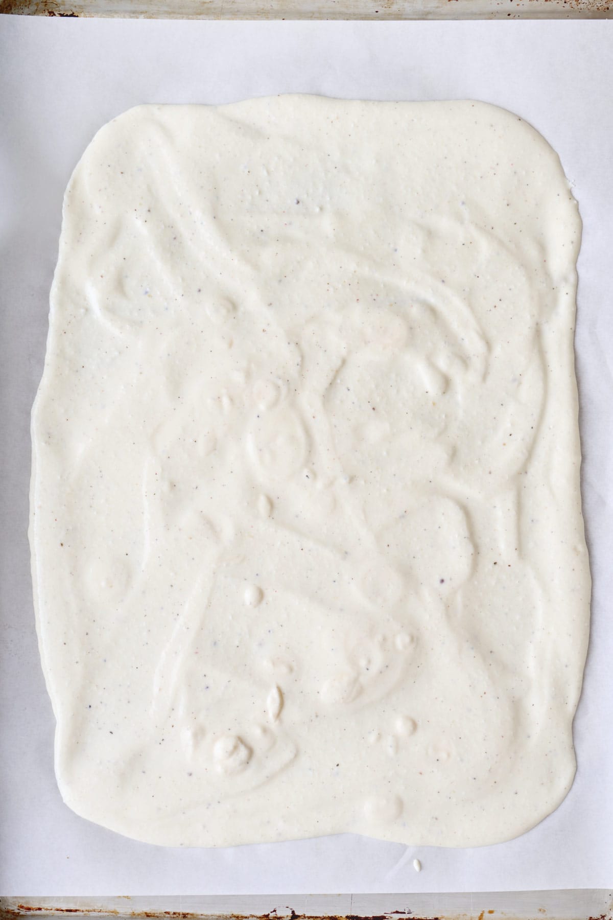 Cottage cheese mixture spread on a parchment lined baking sheet before baking.