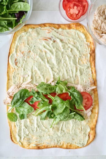 Cottage cheese flatbread with yogurt pesto sauce, chicken, tomatoes, and mixed greens before rolling.