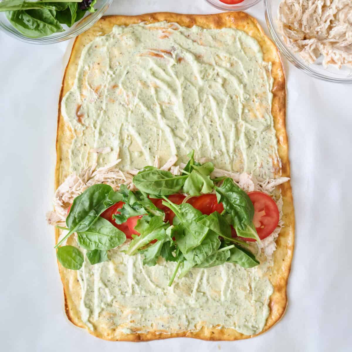 Flatbread with yogurt pesto sauce, chicken, tomatoes, and mixed greens before rolling.