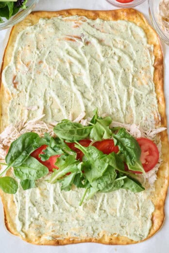 Flatbread with yogurt pesto sauce, chicken, tomatoes, and mixed greens before rolling.