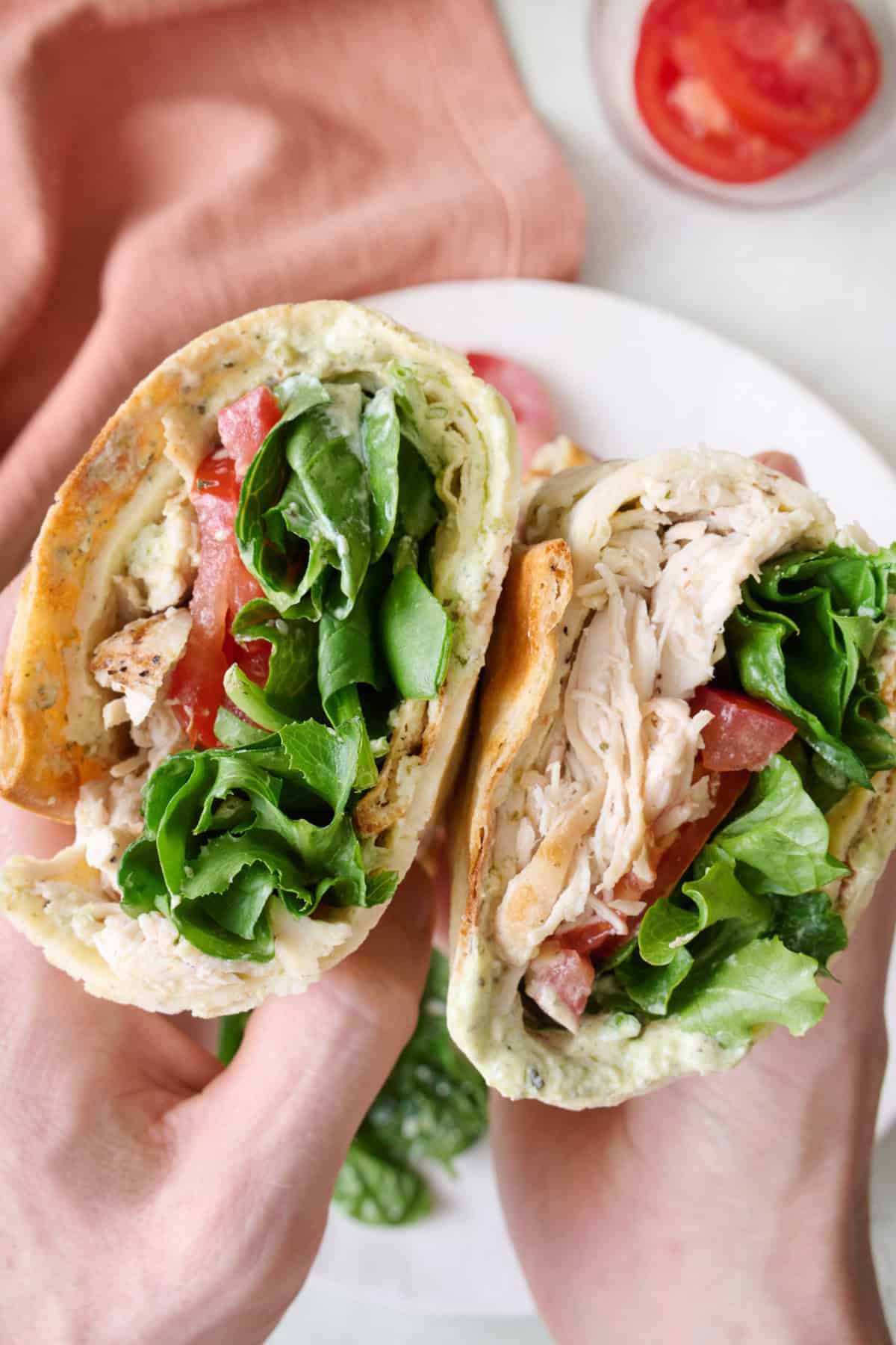 Cottage cheese flatbread rolled up and stuffed with chicken, tomatoes, and mixed greens split in half with cut side forward to show filling.