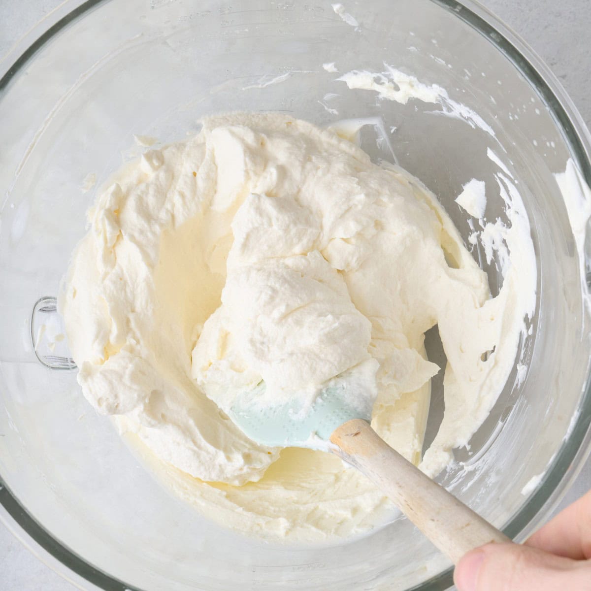 Whipped cream added on top of smooth cream cheese and folding together with a rubber silicone spatula.