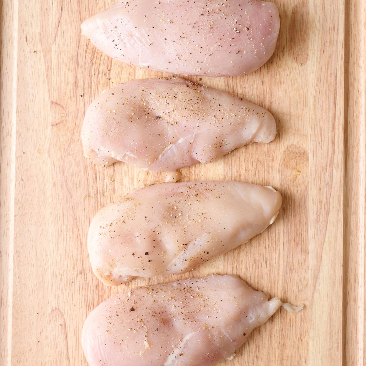 Seasoned uncooked chicken breast on a cutting board.