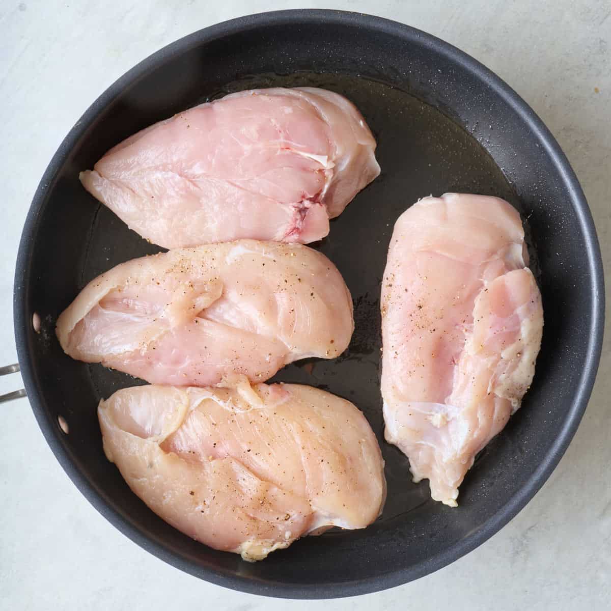 Seasoned chicken breasts in a skillet before cooking.