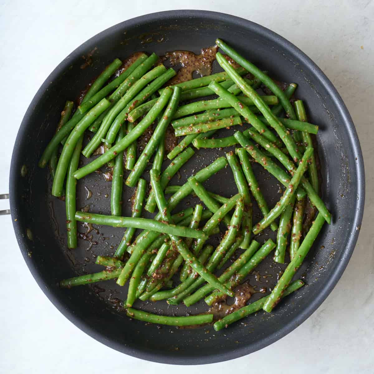 Green beans in a skillet with remaining sauce from recipe.