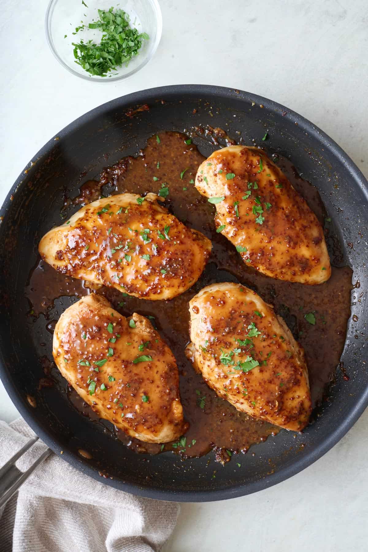 Honey mustard chicken breasts in a skillet with extra sauce.