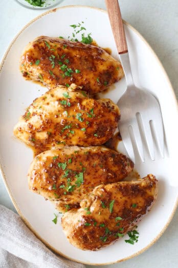 Honey mustard chicken breasts on a platter with a large serving fork.