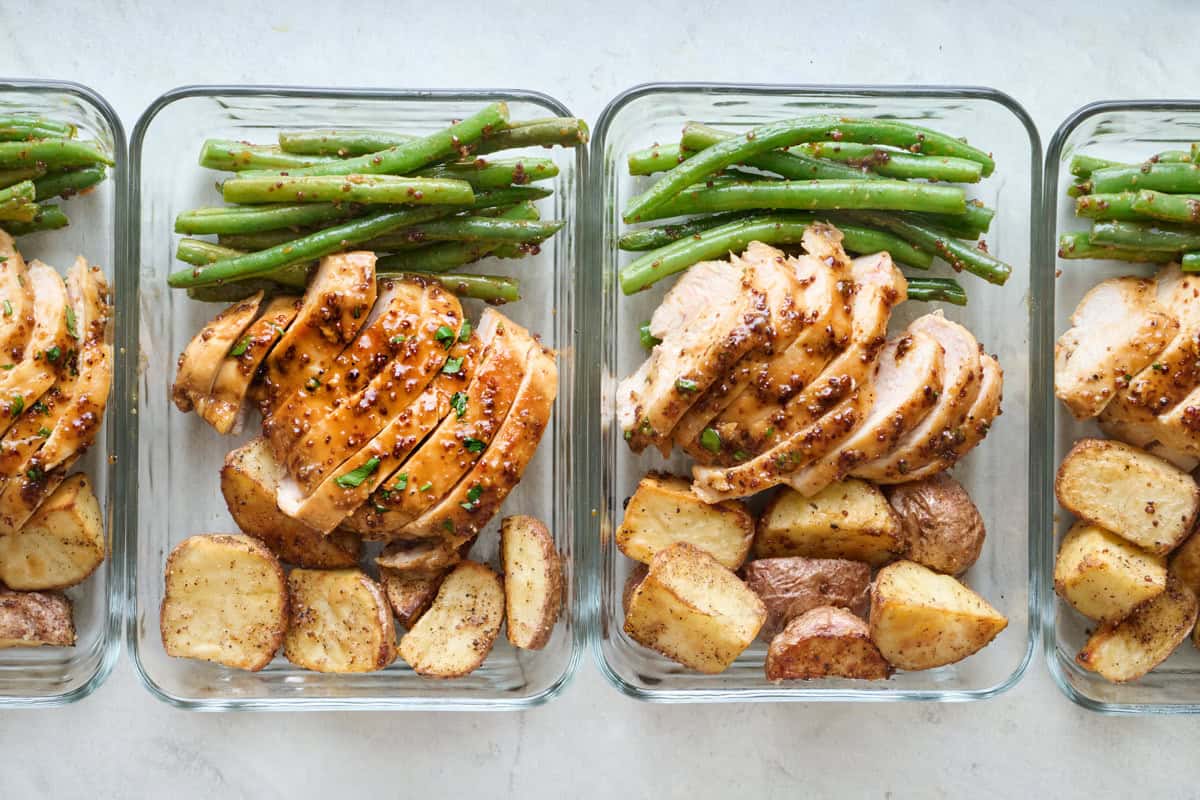 Sliced honey mustard chicken, potatoes, and green beans divided into 4 meal prep containers.