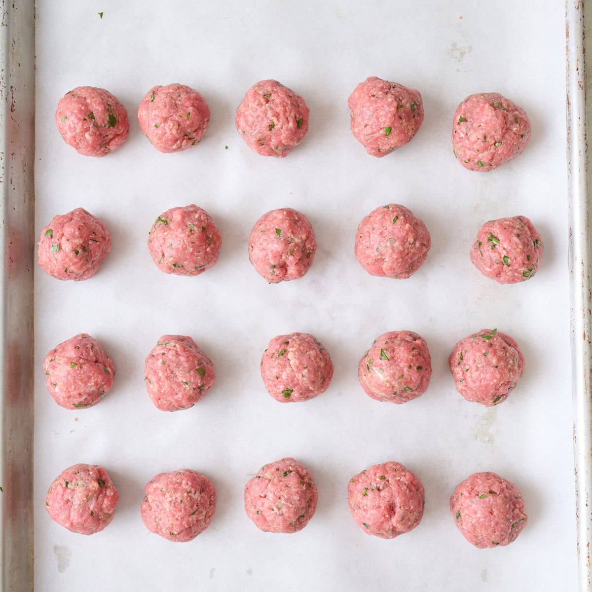 Meat balls on a parchment lined baking sheet.