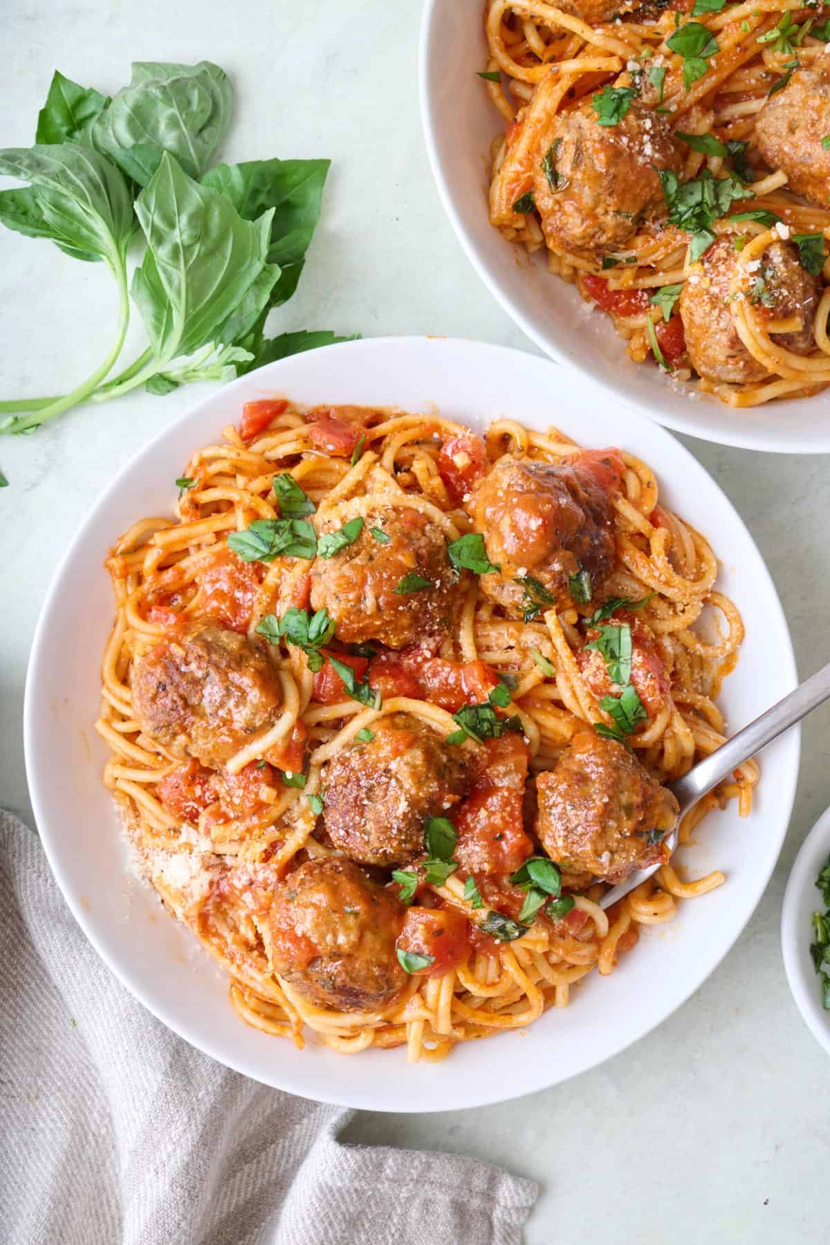 Instant pot spaghetti and meatballs in two shallow bowls garnished with fresh basil and grated parmesan cheese with a fork dipped into bowl.