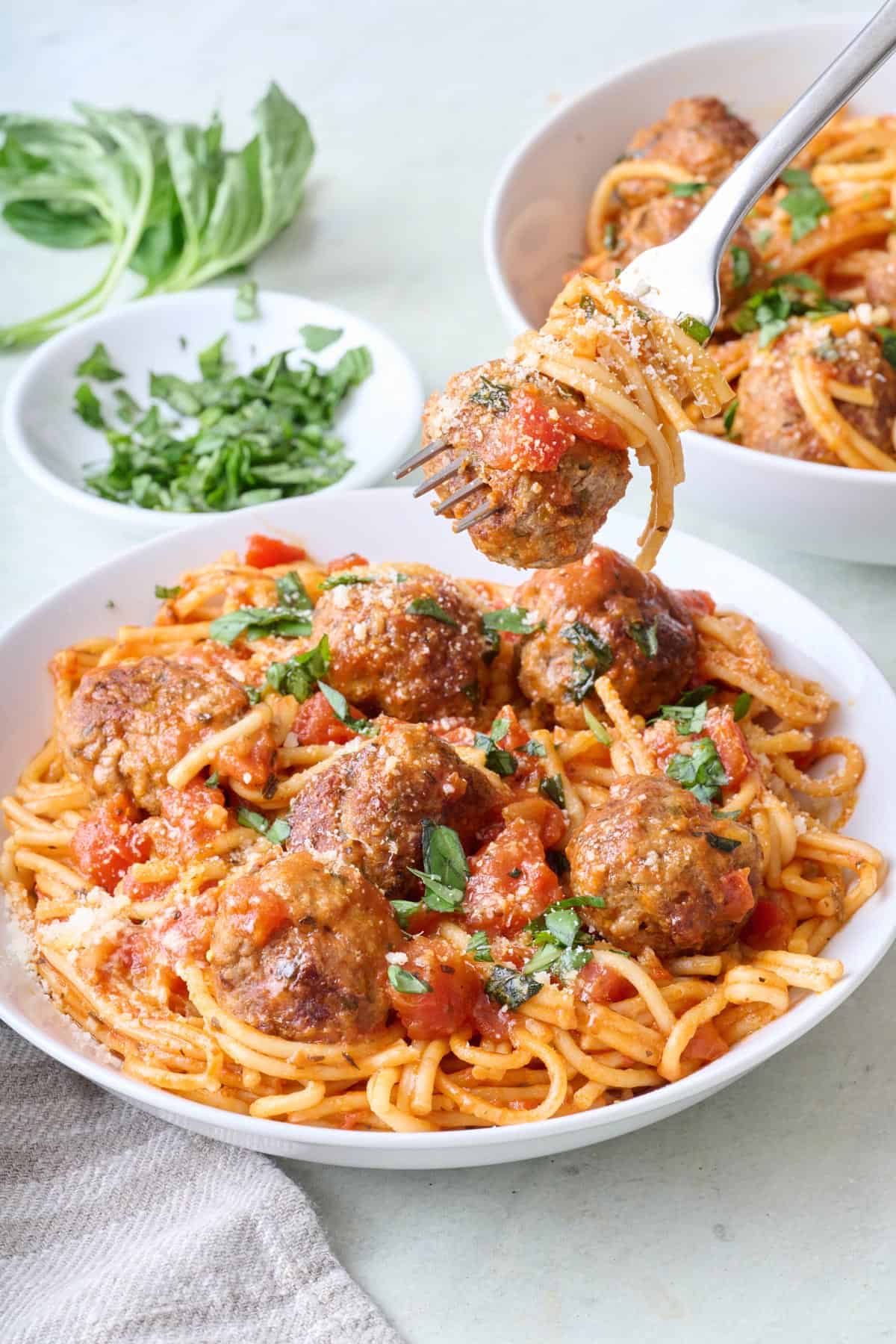 Fork lifting up a bite of spaghetti with a meatball on it over a bowl of pasta.