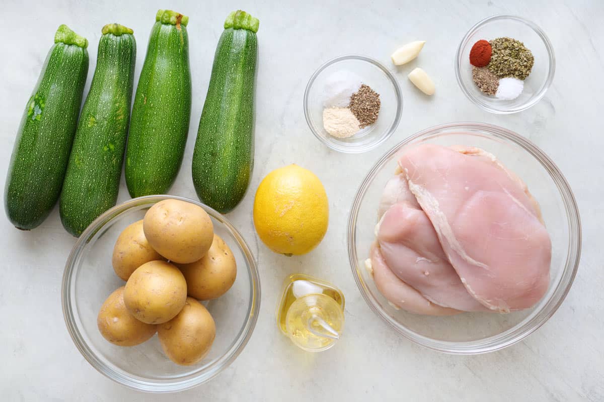 Ingredients for recipe: zucchini, potatoes, lemon, oil, seasonings, garlic, and chicken breasts.